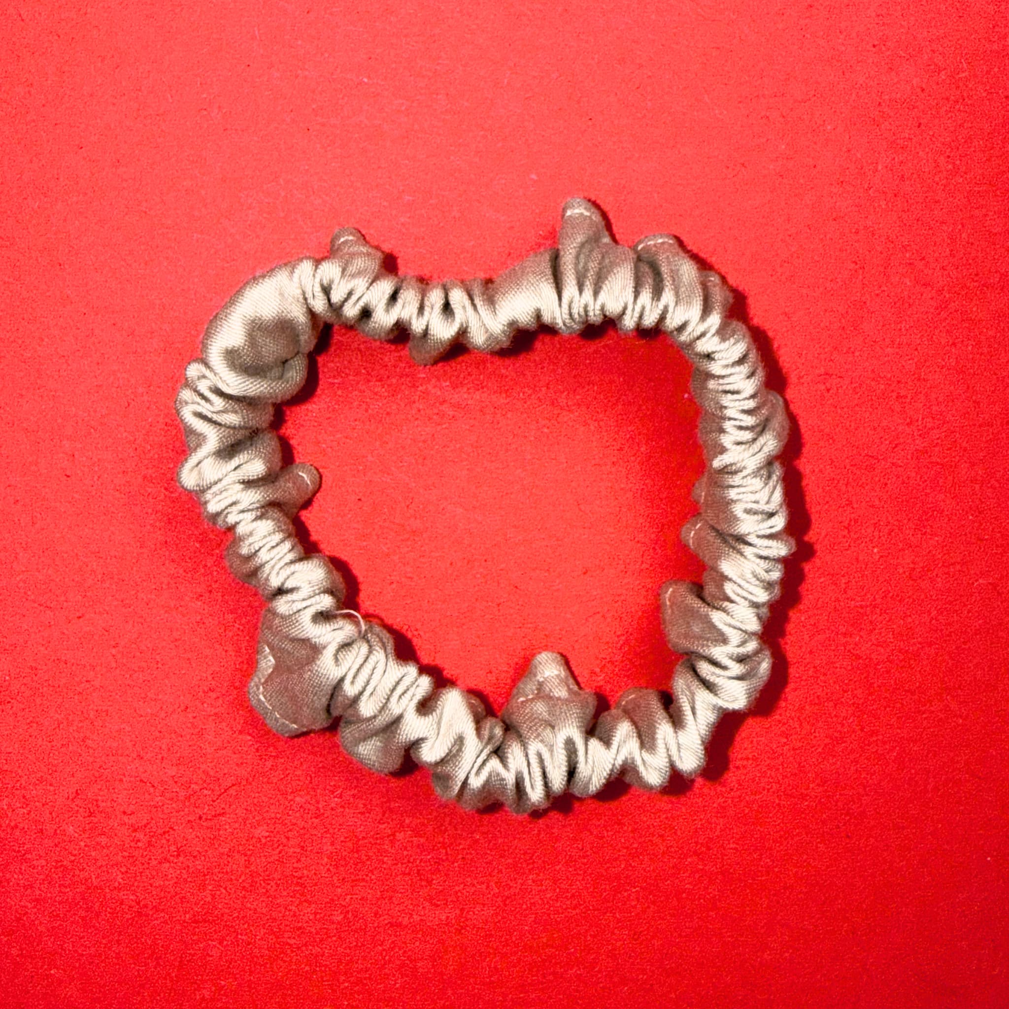 Scrunchie Mini béžově zlatá od Hecatoo™ složená do tvaru srdce –ručně šitá gumička ze 100% bavlněného saténu. Teplý zlatavý odstín který rozzáří každý outfit.